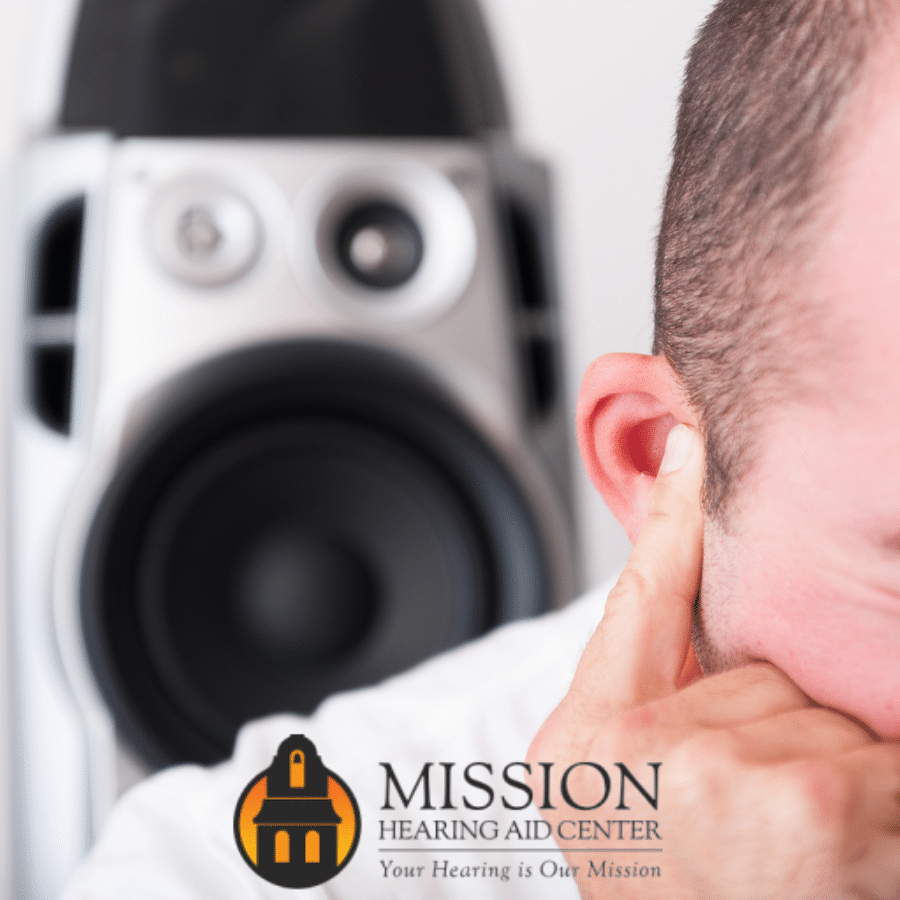 A man holding his ears in pain while a speaker right behind him plays very loud music.